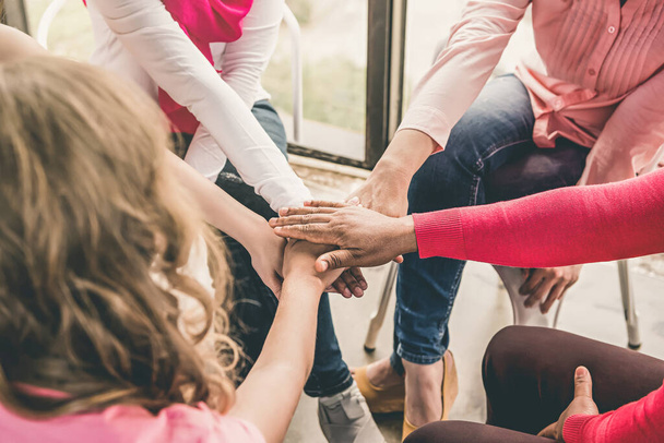 Multiethnische Frauen in pinkfarbener Kleidung legen ihre Hände zusammen, um sich gegenseitig bei einem Treffen zur Sensibilisierung für Brustkrebs zu stärken - Foto, Bild