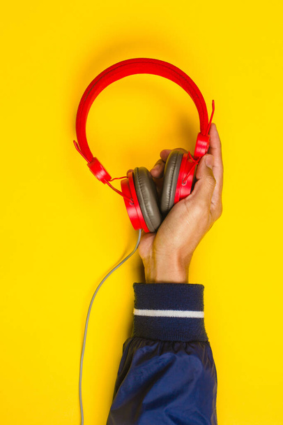 hand holding Red headphones on yellow background. Music concept - Valokuva, kuva