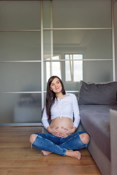 Beautiful pregnant girl is sitting on the floor. - Photo, Image