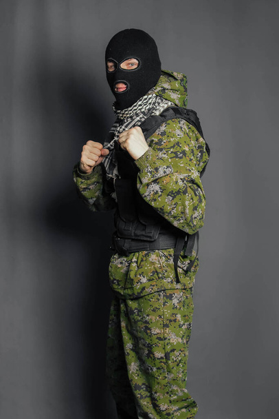 Muž v maskáčích a neprůstřelné vestě s balaklavou na hlavě. Voják zvláštní jednotky, moderní válečník. Fotografie na šedém pozadí, studio. - Fotografie, Obrázek