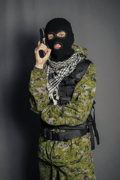 Een lid van de speciale politie, richt, houdt een pistool vast. Gekleed in een bivakmuts, camouflage uniform, kogelvrij vest. Speciale wapens en tactieken. Special Forces.SWAT. - Foto, afbeelding