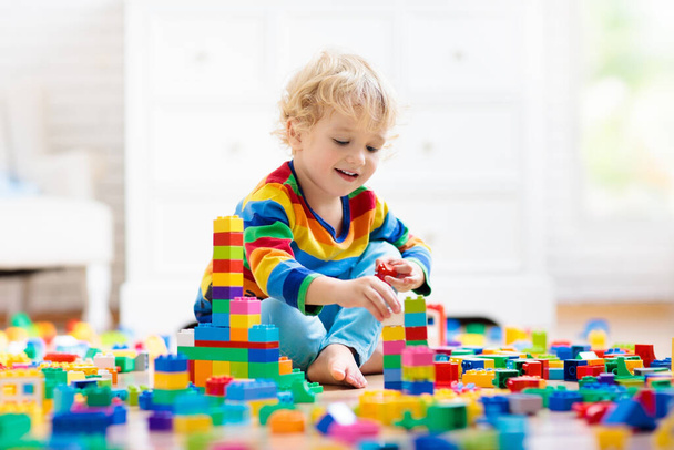 Child playing with colorful toy blocks. Little boy building tower at home or day care. Educational toys for young children. Construction block for baby or toddler kid. Mess in kindergarten play room. - Фото, изображение