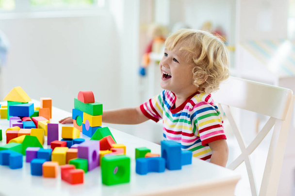 Kind spelen met kleurrijke speelgoed blokken. Kleine jongen die een toren van blokspeelgoed bouwt. Educatief en creatief speelgoed en spelletjes voor jonge kinderen. Baby in witte slaapkamer met regenboog bakstenen. Kind thuis. - Foto, afbeelding