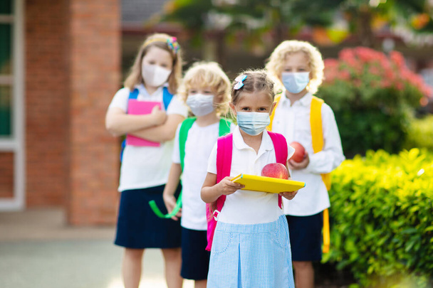 Uczennica nosząca maskę podczas epidemii wirusa korony i grypy. Chłopiec i dziewczynka wracają do szkoły po kwarantannie i zamknięciu. Grupa dzieci w maskach do zapobiegania koronawirusom.  - Zdjęcie, obraz