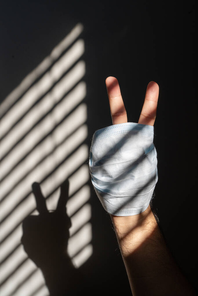 Рука показывает знак победы с медицинской маской. Концепция COVID-19
. - Фото, изображение