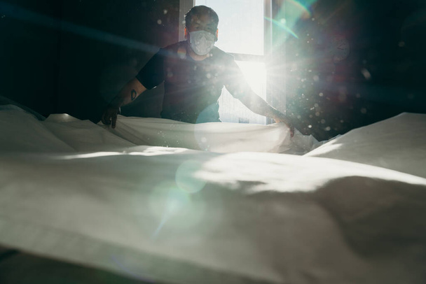Asian man cleaning bed in morning. House keeping action. Bedroom gainst the sun light. - Фото, изображение