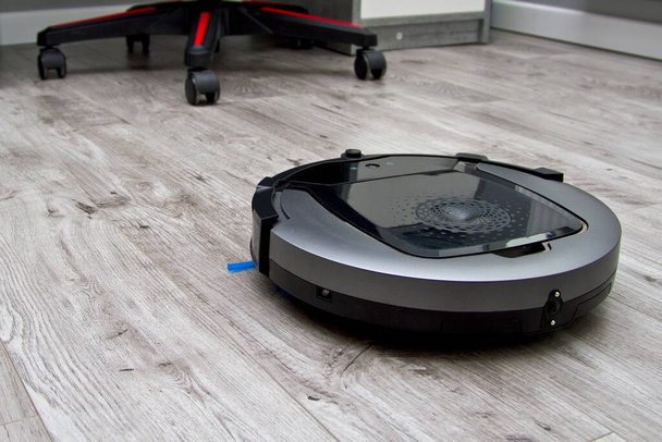 Рабочий роботизированный пылесос на деревянном полу с ламинатом в пустой комнате
 - Фото, изображение