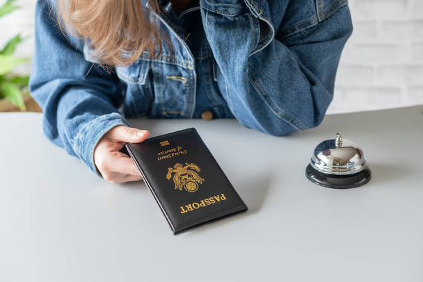 Woman using American passport for registration in the hotel. Silver vintage bell on reception desk. Hotel service.  - Fotoğraf, Görsel