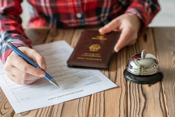 Woman using Germany passport filling hotel reservation form in the hotel. Silver vintage bell on wooden rustic reception desk. Hotel service.  - Valokuva, kuva