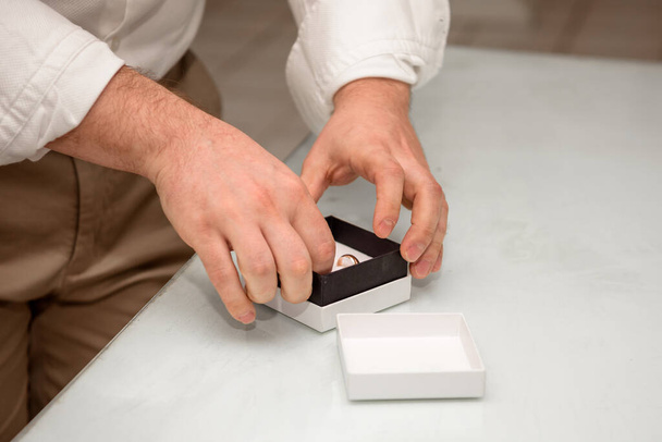 Ένας άντρας με λευκό πουκάμισο βγάζει δαχτυλίδια από ένα κουτί.. - Φωτογραφία, εικόνα