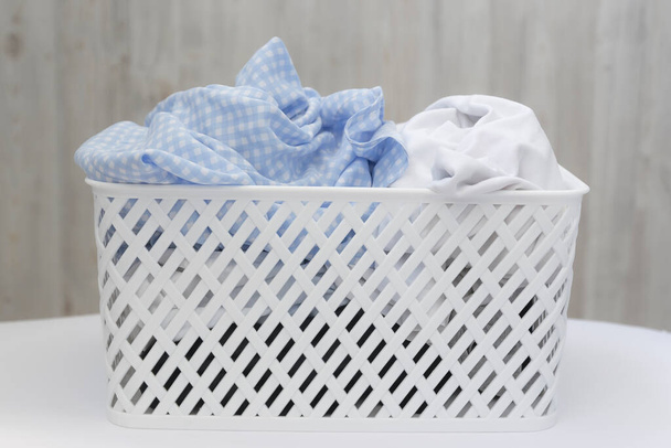 Blue and white dirty things in a white plastic laundry basket on a gray wall background. Washing, home cleaning - Φωτογραφία, εικόνα