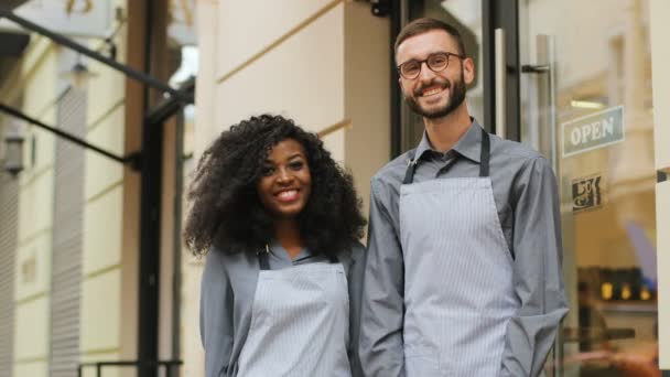 Portrait of young african woman and caucasian man, working in the cafe, crossing arms and smiling on camera outside the cafe. - Video