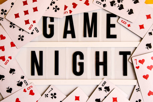 Game night text na světelné skříňce s hracími kartami na žlutém pozadí, stolní hry, deskové hry a Scrabble písmena na žlutém pozadí hláskovací slova HERNÍ NIGHT - Fotografie, Obrázek