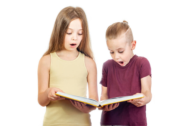 Mladý překvapený roztomilý dívka a chlapec se dívají na žlutou knihu izolované na bílém pozadí - Fotografie, Obrázek