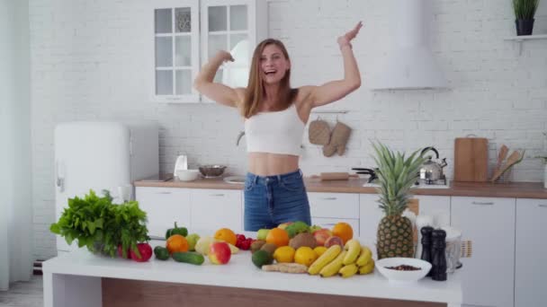 Happy young female in the kitchen. Beautiful lady throws away centimeter and takes banana. Fresh fruit and vegetables on the table. Healthy diet. - 映像、動画