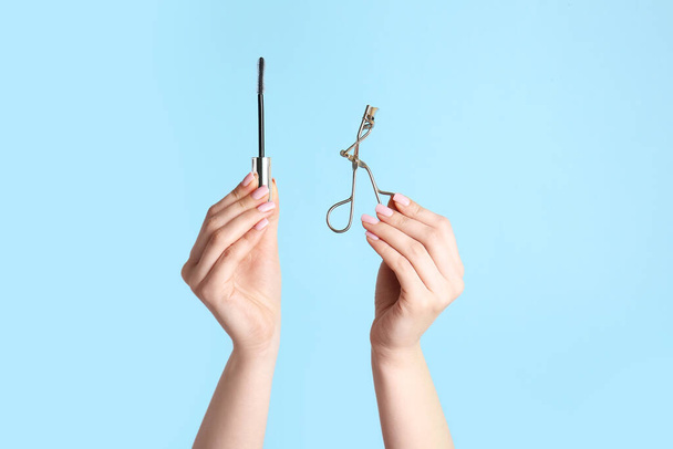 Female hands with mascara and eyelash curler on color background - Photo, Image