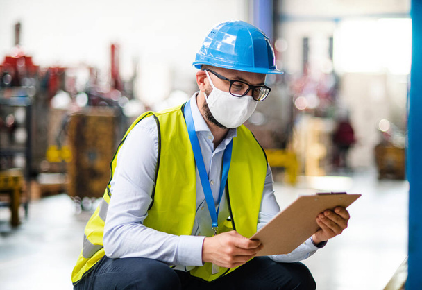 Technician or engineer with protective mask and helmet working in industrial factory. - Photo, image
