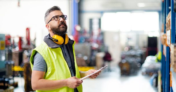 Technician or engineer with protective headphones standing in industrial factory. - Фото, изображение