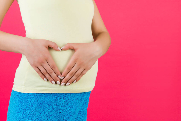 Крупным планом молодая беременная женщина придает форму сердцу с руками на животе на розовом фоне. С любовью к будущему ребенку. Копирование пространства
. - Фото, изображение