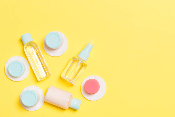 Set of travel size cosmetic bottles on yellow background. Flat lay of cream jars. Top view of bodycare style concept. - Photo, Image