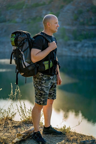 Tourist with a backpack on his shoulders stands on a rock. Summer nature background. A traveler looks at the landscape in front of him - Foto, Imagen