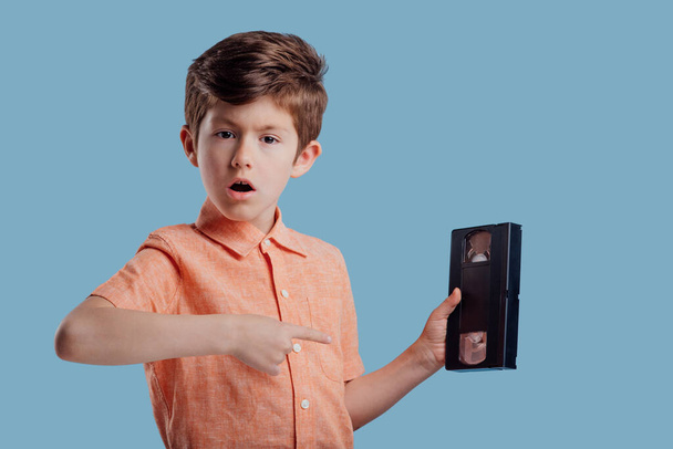 Surprised boy showing video cassette on blue background - Φωτογραφία, εικόνα