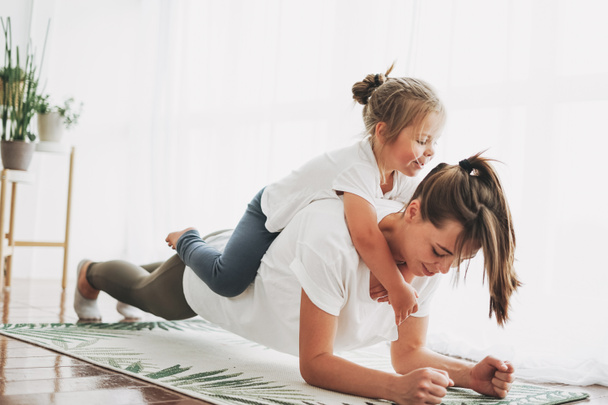 Happy mom and little daughter doing yoga morning exercise together at bright interior home - Foto, Imagen
