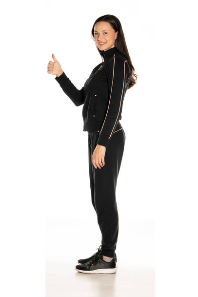 Вид збоку молодої жінки в чорному костюмі, що показує великі пальці вгору на білому тлі
 - Фото, зображення