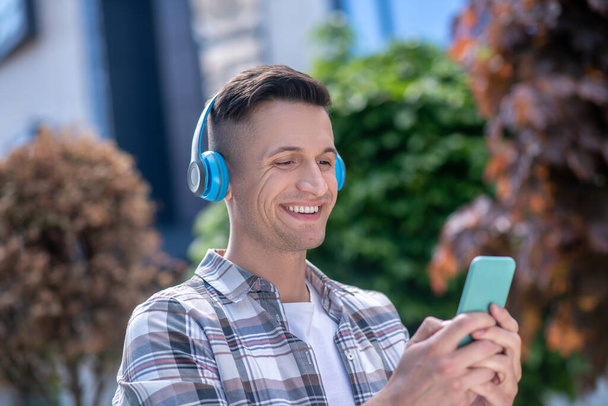 Cheerful dark-haired male wearing headphones, chatting on the phone - Zdjęcie, obraz