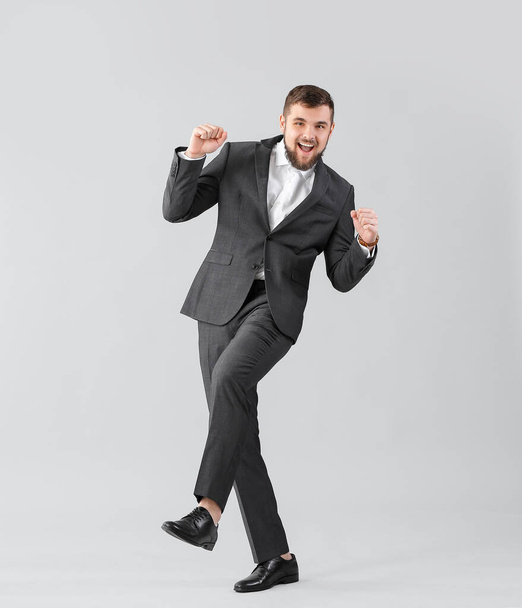 Handsome young businessman dancing against light background - Foto, afbeelding