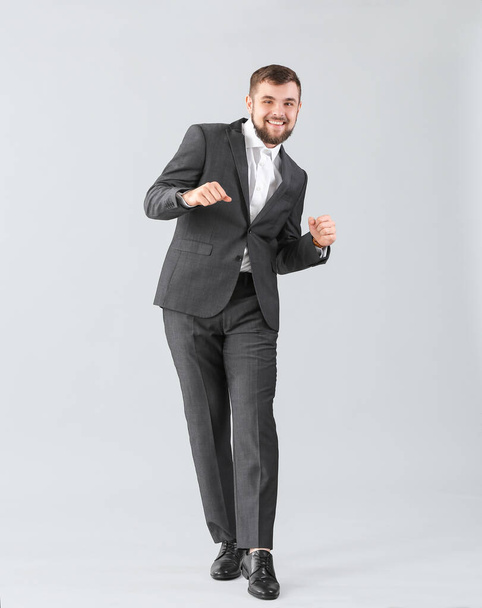 Schöner junger Geschäftsmann tanzt vor hellem Hintergrund - Foto, Bild