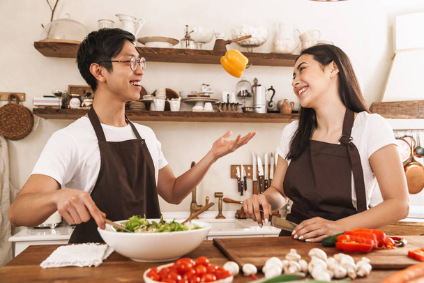 Image of excited multicultural couple in aprons laughing and making lunch at cozy kitchen - Foto, immagini