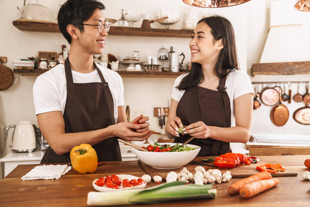 Image of multicultural couple smiling and looking on you while cooking dinner in cozy kitchen - Foto, immagini