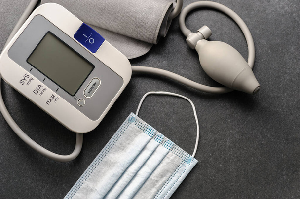 Blutdruckmessgerät mit medizinischer Einmalmaske auf einem dunklen Tisch - Foto, Bild