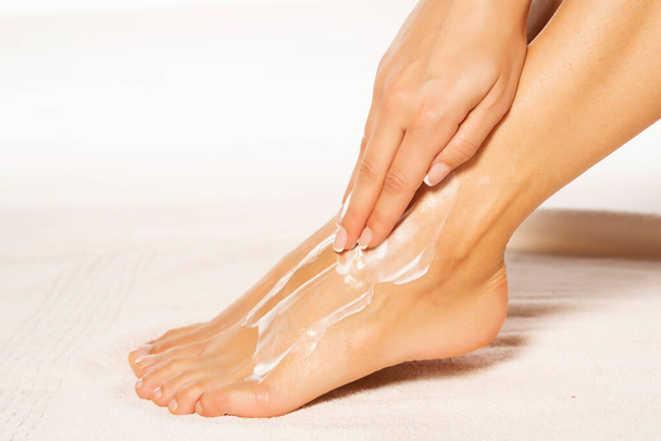 a young woman applies lotion to her feet on white towel - 写真・画像