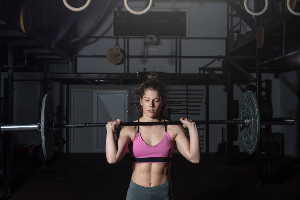 Young strong muscular fit girl with big muscles preparing for hard strength weight lifting or dead lift cross workout training with barbell weights in the gym real people exercising - 写真・画像