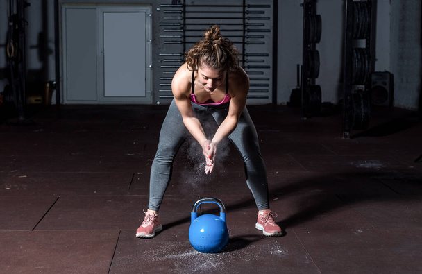Young fit muscular strong girl preparing putting sport chalk on her hands for heavy kettlebell cross swing workout training in the gym with clap  or clapping hands real people exercise - Foto, afbeelding