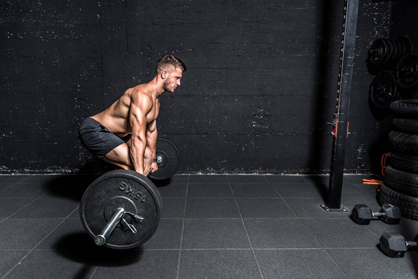 Young strong fit muscular sweaty man with big muscles doing barbell weight lifting cross training workout in the gym dark image real people - 写真・画像