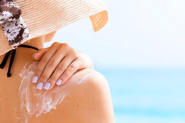 Sunscreen sunblock. Woman in a hat putting solar cream on shoulder outdoors under sunshine on beautiful summer day. - Photo, Image