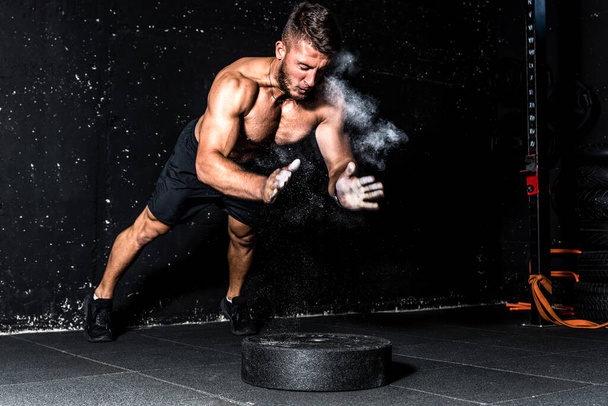Young fit muscular man with big sweaty muscles doing push ups cross workout training with clap his hand above the barbell weight plate on the gym floor with motion blur - Photo, Image