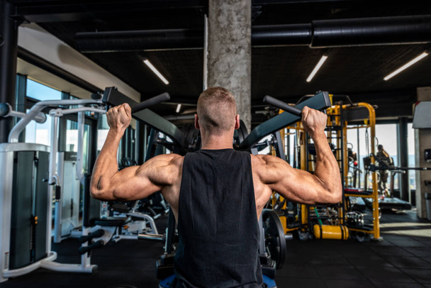 Young strong muscular sweaty fit bodybuilder man back muscles workout training in the gym on the machine - Fotoğraf, Görsel