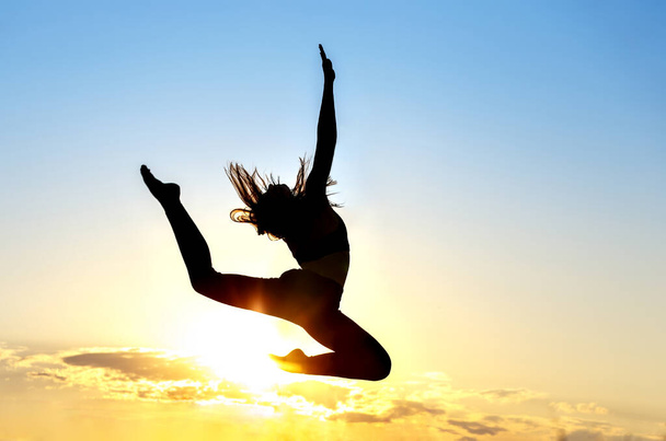 Graceful gymnast dancer jumping leaps against sunset - Photo, image