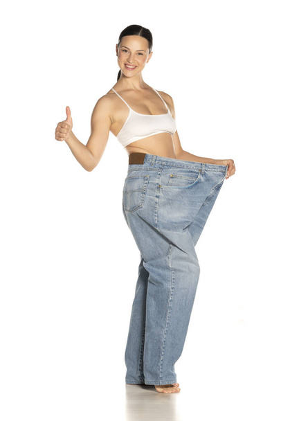 Young slim woman in big size pants showing thumbs up - Zdjęcie, obraz