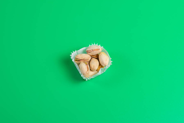 A serving of pistachios in a paper muffin cup on a green background. - Fotografie, Obrázek