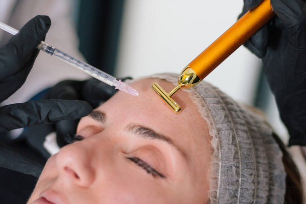 Esthetische geneeskunde behandeling concept. close-up zicht op jonge vrouw krijgen cosmetische injectie van botulinum toxine in het voorhoofd. - Foto, afbeelding