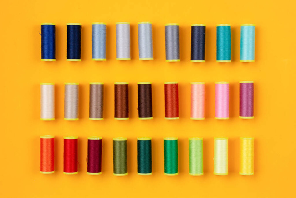 Sewing threads of many colors arranged neatly on an orange background - Foto, Imagem