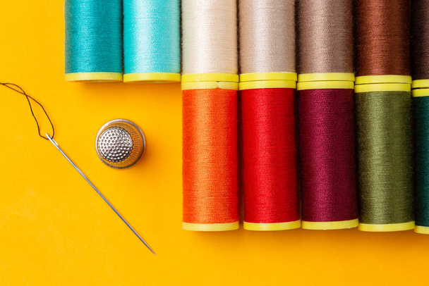 Naaien van draden van vele kleuren en een naald vingerhoedje netjes geplaatst op een oranje achtergrond - Foto, afbeelding