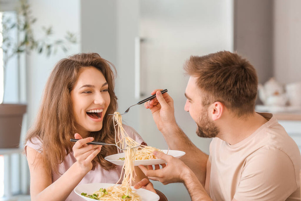 Ευτυχισμένο νεαρό ζευγάρι τρώει μεσημεριανό στην κουζίνα - Φωτογραφία, εικόνα