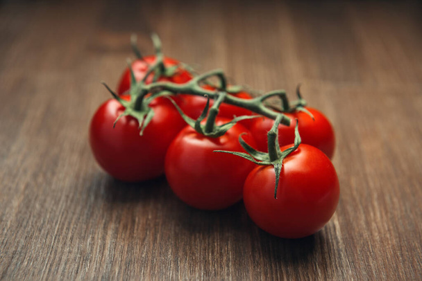Truss červených cherry rajčat na dřevěném stole, detailní parta malých kulatých rajčat na stole - Fotografie, Obrázek