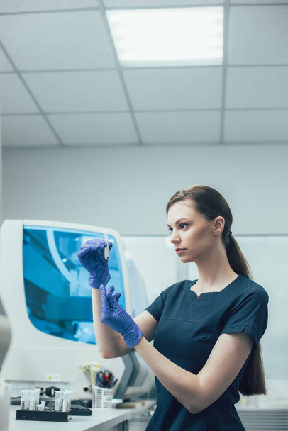 Technicien de laboratoire prudent portant des gants en caoutchouc et regardant le liquide transparent dans une éprouvette
 - Photo, image